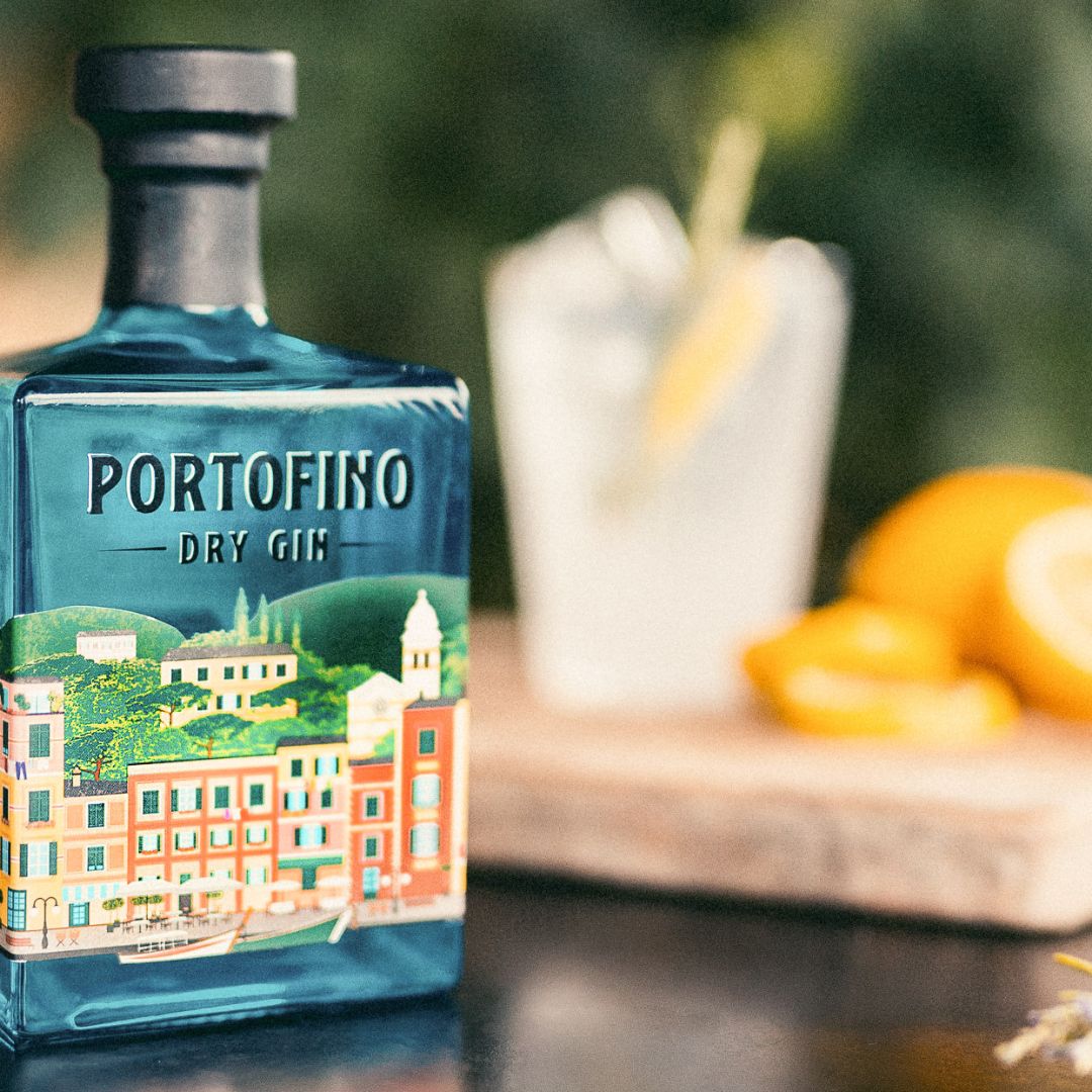 Pierwszoplanowo butelka Portofino Dry Gin, na rozmazanym tle drink i cytryny