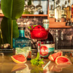 Portofino Dry Gin and Pampelle Aperitif liqueur bottles with a spritz cocktail on an elegant bar counter.