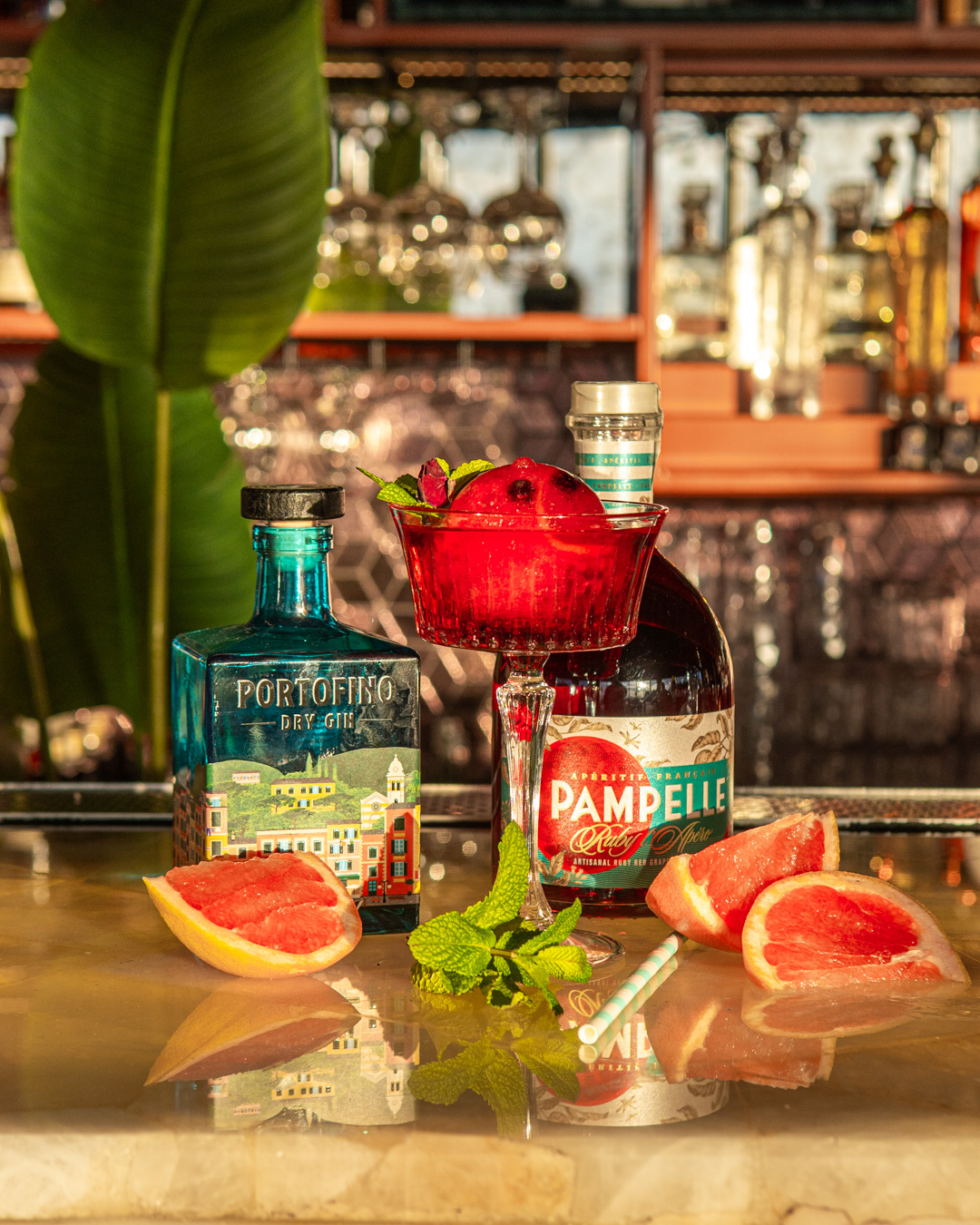 Portofino Dry Gin and Pampelle Aperitif liqueur bottles with a spritz cocktail on an elegant bar counter.