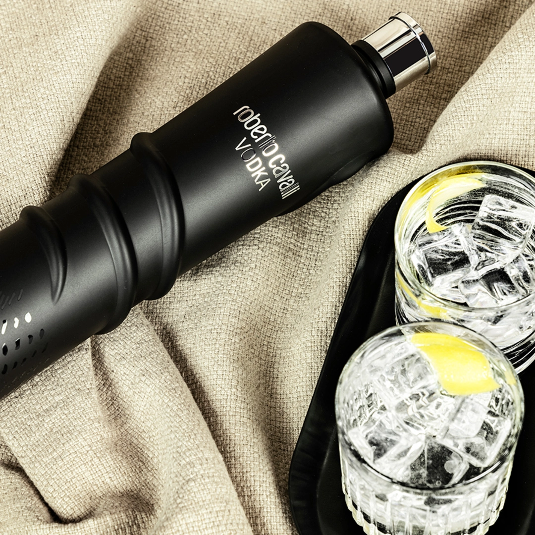 Butelka Roberto Cavalli Vodka Night Edition na tkaninie obok dwóch szklanek z lodem i cytryną