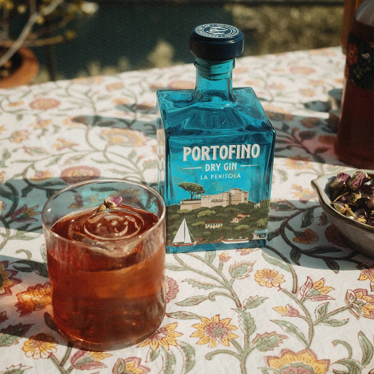 Butelka ginu Portofino Dry Gin La Penisola obok szklanki z drinkiem