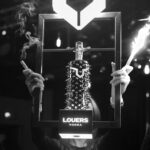 Two hands with sparklers holding a presenter on a LOUERS® bottle with smoke.