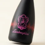 A black, matte bottle of Lamborghini DJ Luminous Brut wine with a distinct, pink-illuminated Lamborghini logo and a sound wave motif on a light background.