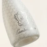 Close-up of a white bottle of Lamborghini Ice Brut wine. A delicate geometric pattern and a luxury silver Lamborghini logo are visible