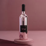 Jasnoróżowa, metaliczna butelka wina Lamborghini Luxe Rosé wyeksponowana na małym, okrągłym podeście na minimalistycznym, bordowo-różowym, studyjnym tle.