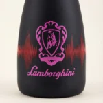 Macro shot of the front of a black Lamborghini DJ Luminous Brut bottle. In the center is a pink-illuminated Lamborghini bull shield logo, against a background graphic resembling an equalizer sound wave