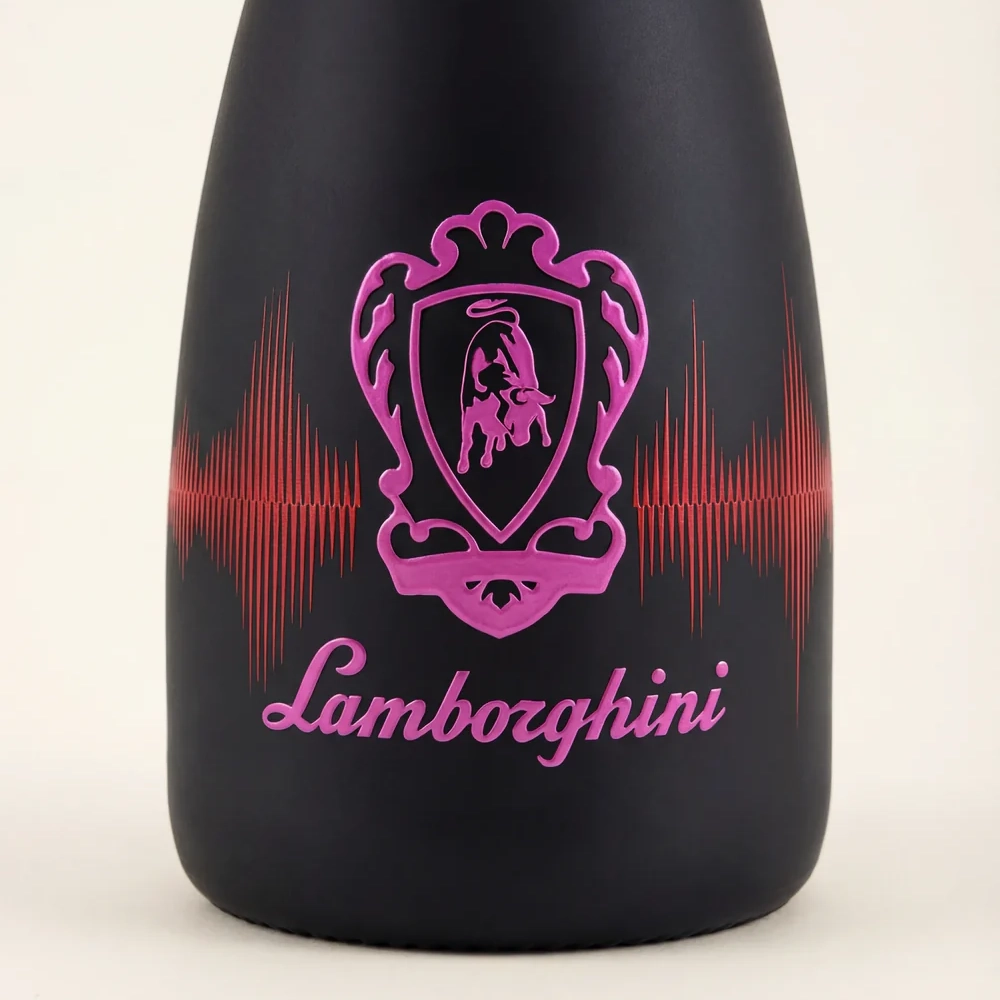 Macro shot of the front of a black Lamborghini DJ Luminous Brut bottle. In the center is a pink-illuminated Lamborghini bull shield logo, against a background graphic resembling an equalizer sound wave