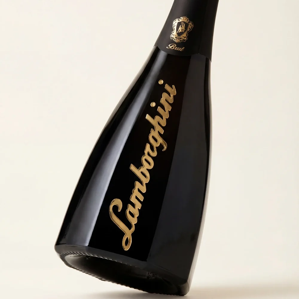 A minimalist shot showing the lower part and profile of the geometric black bottle of Lamborghini Ottagonale Brut Gold wine. The bottle is slightly tilted, exposing the gold logo and the octagonal base.