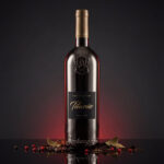 A dark metallic bottle of Lamborghini Luxe Titanio red wine, surrounded by peppercorns and bay leaves on a black background with red illumination.
