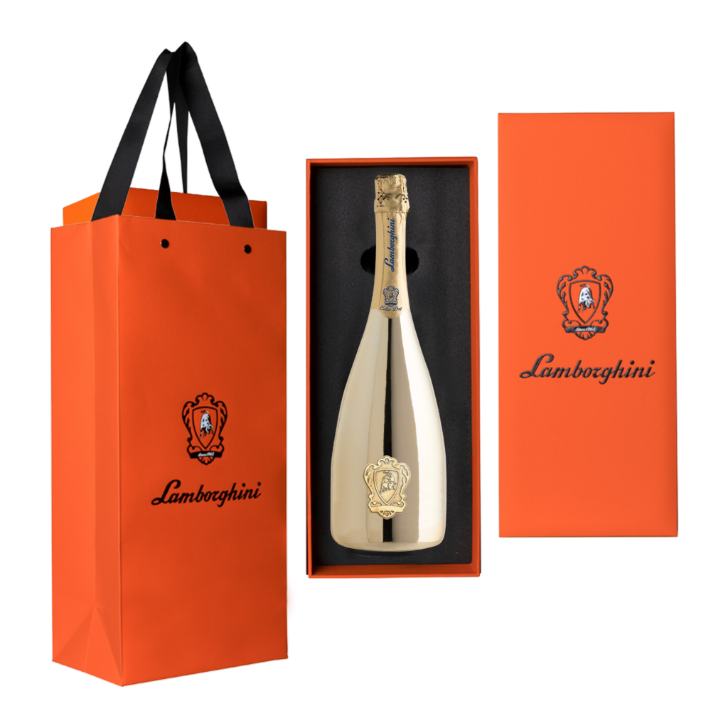 A gold, mirrored bottle of Lamborghini Extra Dry Gold wine in an open, vertical orange gift box next to an exclusive Lamborghini gift bag on a black background.
