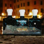 Trzy butelki Portofino Dry Gin Winter Nights Limited Edition ustawione obok siebie, ukazujące zimową panoramę Portofino.
